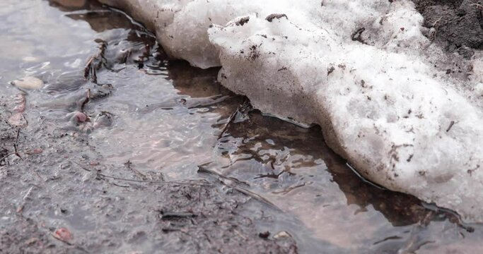 A stream with meltwater and mud flows in the spring along a country road path.