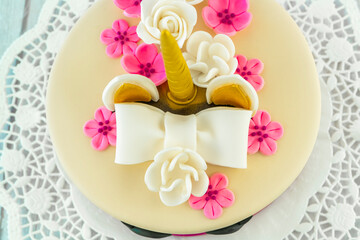 Flat lay Unicorn cake on a wooden background and lace. Cute unicorn layered homemade cake decorated with bow, rose flowers, golden corn and ears