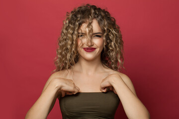 Happy funny smiling woman with long healthy curly hair on red background. Pretty model with trendy styling and hair dye
