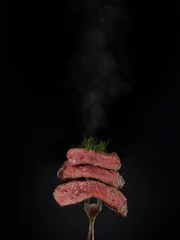 Poster Steak menu. Grilled hot pieces of beef steak medium rare with smoke on fork on black background. © Dmitriy Melnikov