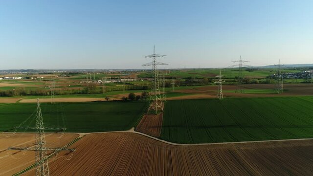 Electric supports against the sky among empty green and yellow square fields. The civilization is visable on the background, cars are driving on a asphalt road. Sunny day, summer, countryside, high vo