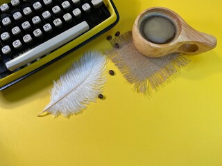 on a yellow background there is a typewriter Jerzy with an ostrich feather. Next to it is a wooden cup with coffee and scattered coffee beans