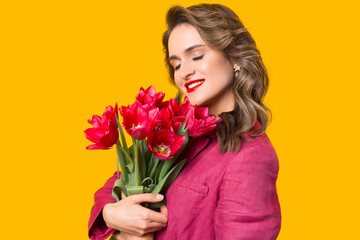 Close up portrait of a young beautiful woman holding some magenta tulips near her face.