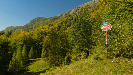 Fototapeta na wymiar Hiking into Buila Mountains. A guide sign tells the times needed until reaching the mountain peaks. Carpathia, Romania.