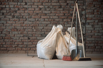 Shovel, broom and bags with a construction garbage on the dusty construction site floor background.