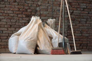 Shovel, broom and bags with a construction garbage on the dusty construction site floor background.