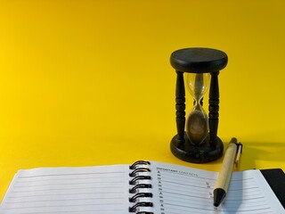 On a yellow background there is an hourglass measuring the time, next to it is a pen and an open notebook