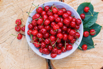 Red cherries in a plate on a tree stump with a crack and tree rings texture. Fresh summer harvest.