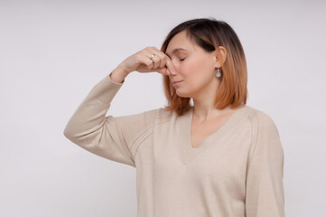  Young woman feels disgust pinches her nose with fingers because of unpleasant stink.