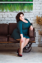 Plus size fashion model in green dress in the interior, fat woman at home