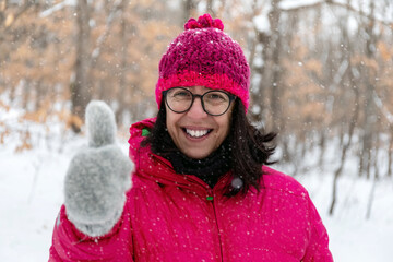 Portrait of a woman in the snowy forest, dressed in mountain clothes, gloves and a wool hat, she smiles happily and with her hands makes the ok sign.