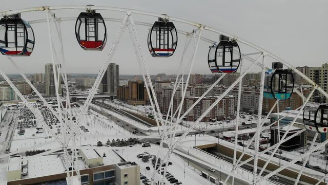 Rotating Ferris wheel in Tatarstan Kazan at winter. Snow covered pool under near aquapark. Aerial drone view. Flying over. Drone is standing