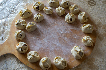 Uncooked russian pelmeni on cutting board and ingredients for homemade pelmeni on white table. Process of making pelmeni, ravioli or dumplings with meat. Raw meat in dough on a cutting board