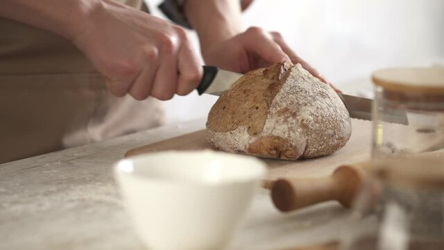 Cuts home baked bread, organic homemade brown cereal bread is cut with a bread knife. Side view of a large palan.