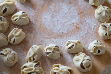 Uncooked russian pelmeni on cutting board and ingredients for homemade pelmeni on white table. Process of making pelmeni, ravioli or dumplings with meat. Raw meat in dough on a cutting board