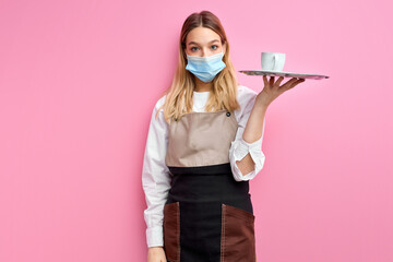 Woman in medical mask holding white classic Cup for coffee or tea on tray