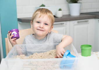 little blonde boy playing with kinetic sand at home. Early age education. Toddler playing