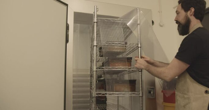 Bearded Male Baker Working In Bakery Carrying Bread Dough Out Of Fridge Wearing Apron