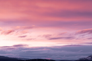 A pink winter sunrise during March with purple pastel scenes in the wilderness of northern Canada with a huge frozen lake below and mountains surrounding. Great for sky replacement use. 