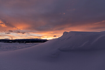 Winter frozen lake scene in northern Canada on a stunning cloudy sunset afternoon in March with white snow, mountains in background and iconic Canadian landscape in the north. 