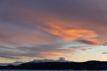 A fiery orange, pink and purple dark sunset seen in northern Canada during winter time season with snow capped mountains and wilderness setting landscape for prints, art, office or home artwork. 