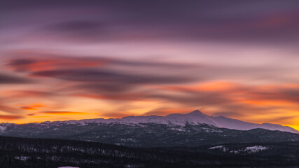 A fiery orange, pink and purple dark sunset seen in northern Canada during winter time season with snow capped mountains and wilderness setting landscape for prints, art, office or home artwork. 