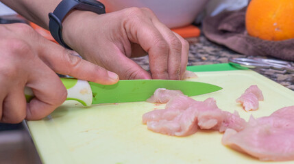 Woman cutting chicken fillets on the board in the kitchen.