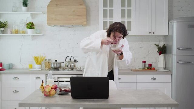 Hurrying young man running in kitchen, eating morning cereals with milk, checking time on watch, and leaving. Modern busy millennial lifestyle. Caucasian guy being late.