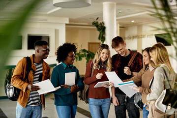 Group of happy students looking at exam results while standing at university hallway. - obrazy, fototapety, plakaty