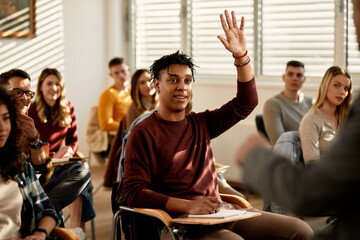 Happy black student raising arm to answer a questing in the classroom.