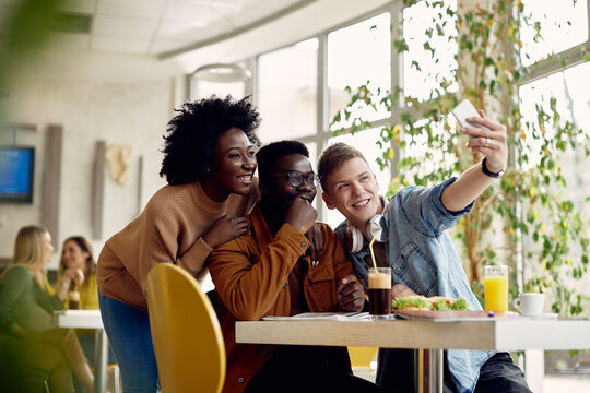 Happy students taking selfie on lunch break in cafeteria.