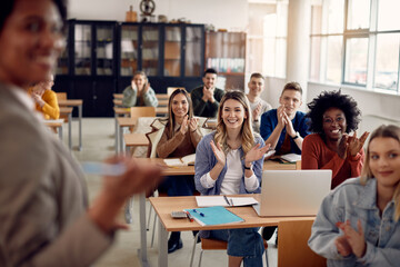 Happy university students applauding to their teacher during lecture in the classroom.