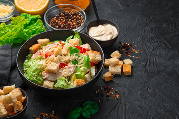 Fresh Caesar salad with sauce, crackers and herbs on a black background.