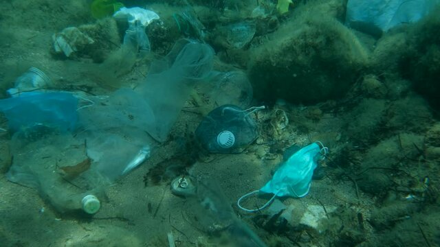 Dead Greater weever fish (Trachinus draco) hitting trapped in plastic bag lies inside plastic bag on the seabed among the medical face mask, plastic and other garbage. Plastic pollution of Ocean.  