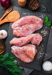Turkey fillet, salt, spices and dill on a black table. Fresh meat, culinary background.