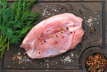 A piece of turkey fillet on a wooden chopping board with salt, spices and dill.