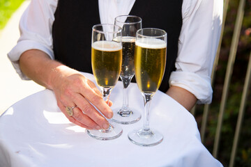 Waiter with black vest and white shirt holding a tray of champagne glasses with hand holding one ready to serve. No face