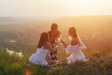 Happy young girlfriends is having picnic on the hill at sunny summer day. 