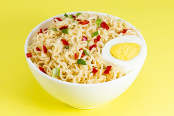 Instant noodles with vegetables and herbs in bowl on yellow background