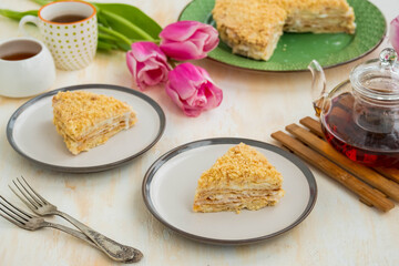 Sliced traditional chopped dough Napoleon cake with custard on a green plate on a light concrete background. Cake recipes.