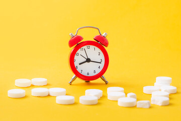Pills, tablets and red alarm clock on yellow background. Medical and health concept in minimal style. Medicine in hospital. Retail drug market.