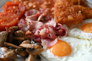 Traditional English Breakfast - plate with fried eggs, beans, mushrooms, bacon, hash browns and...