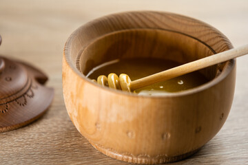 Honey with wooden honey dipper in wooden bowl on wooden table