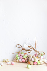 Chocolate Easter eggs, candy in colorful glaze in a transparent bag on a light background. Happy easter. Preparation for the holiday, gift wrapping. Sweet shop, sweet store. Vertical, copy space.