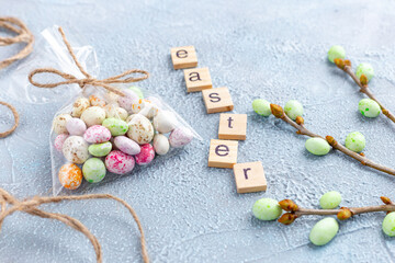 Chocolate Easter eggs in glaze in a transparent bag, branches of a spring tree and wooden letters on a light blue background. Happy Easter time. Preparation for holiday, gift wrapping. Banner.