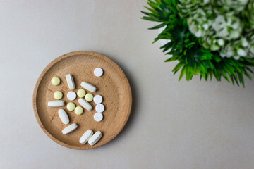 A handful of pills in a wooden plate with green plant. The concept of medcine, treatment. Top view.