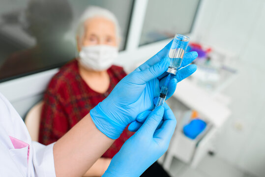 A doctor wearing rubber gloves prepares to inject an elderly woman in the hospital. A nurse holds a syringe before making a vaccine against Covid-19 or coronavirus.