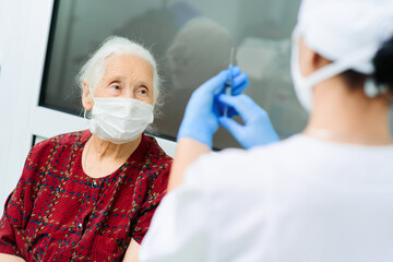 A doctor wearing rubber gloves prepares to inject an elderly woman in the hospital. A nurse holds a syringe before making a vaccine against Covid-19 or coronavirus.