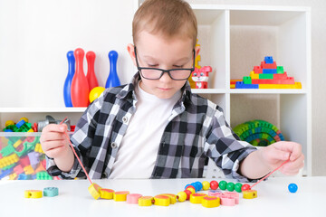 speech therapy, the development of fine motor skills. Toddler boy is stringing beads on a string.