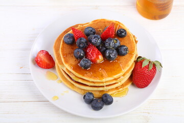 Still life with pancakes, berries and honey on a white background